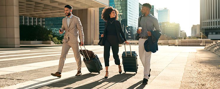 Corporate Relocation Services – Pickfords Removals Three business professionals walking with suitcases through a modern business district during a corporate relocation.